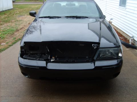 1993 Ford Crown Victoria - Black car's front end is damaged, missing the grille and one headlight assembly.