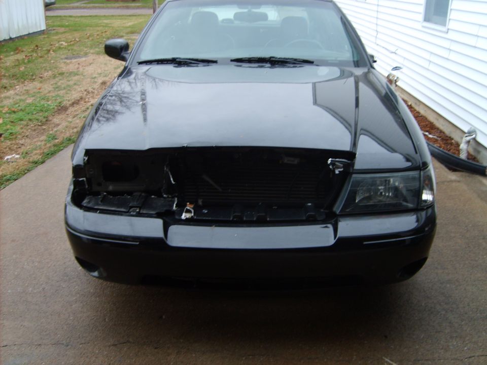 Black sedan front end with bumper and grille removed on a driveway