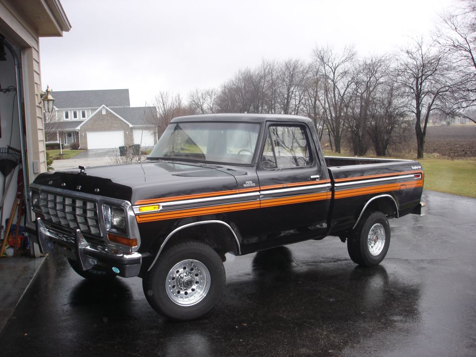 1979 Ford F-150 pickup truck, black with orange side stripes, parked on wet asphalt