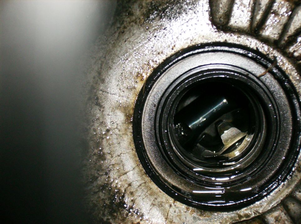 Close-up of a greasy engine part with a circular opening showing internal components