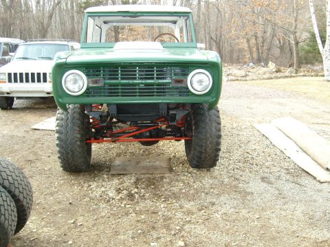 1974 Ford Bronco - Front view of a green 1974 Ford Bronco, lifted with large tires. A white Jeep is visible behind it.