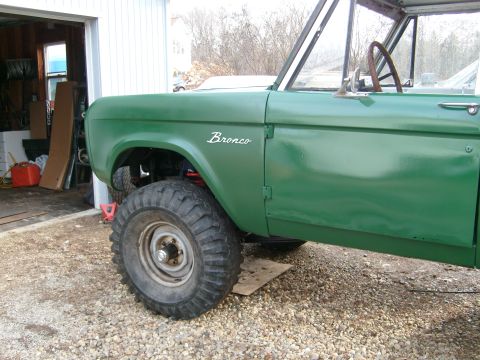 1974 Ford Bronco - A green Ford Bronco is parked in front of a garage, showing its side profile and large tires.