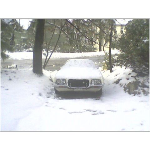 1972 Ford Ranchero - A white car sits covered in snow, its front grille and headlights partially visible.