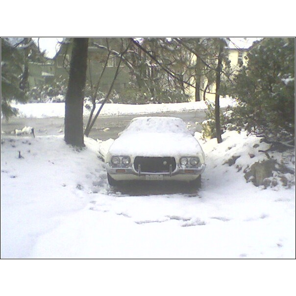 White car with a prominent grille and dual headlights, covered in snow