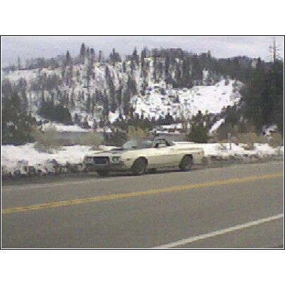 1972 Ford Ranchero - A white coupe with a black hood stripe is parked on the side of a road with snow-covered hills in the background.