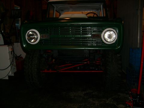 1974 Ford Bronco - The front grille and round headlights of a green 1974 Ford Bronco are visible in this garage photo.