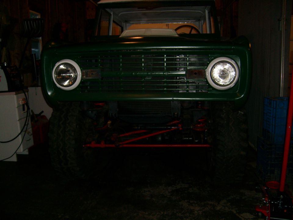 Green 1974 Ford Bronco front view, lifted with large tires, in a garage