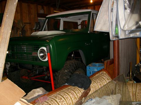 1974 Ford Bronco - A green 1974 Ford Bronco with a white roof is parked indoors, partially obscured by garage clutter.