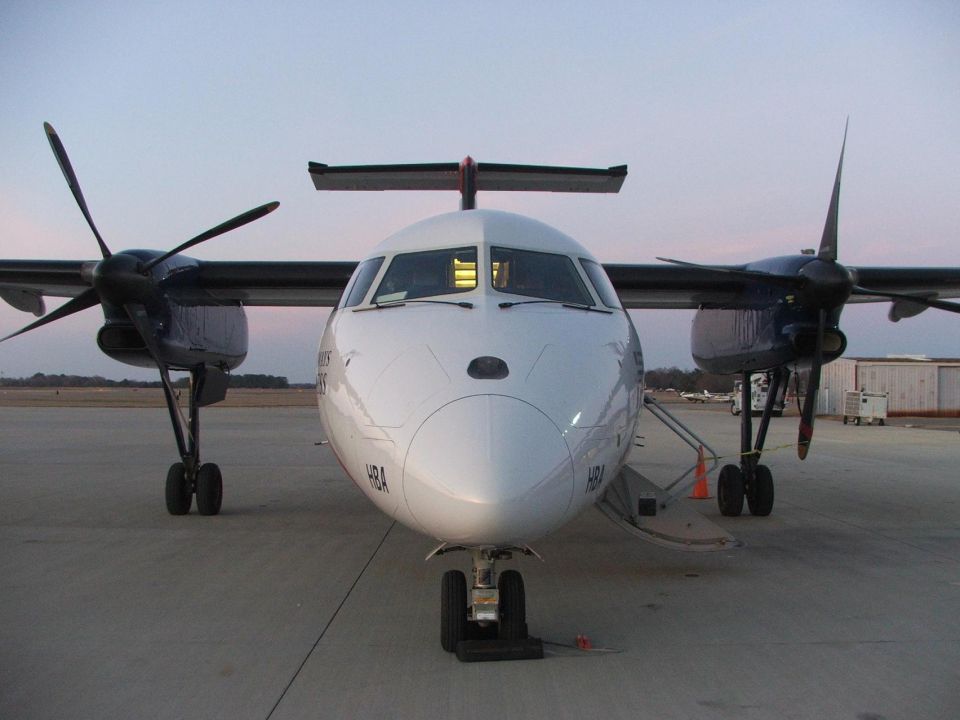 Head-on view of a white twin-turboprop airliner parked on the ramp at dusk