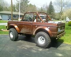 1973 Ford Bronco - Brown 1973 Ford Bronco with a roll cage and off-road tires sits on a paved driveway.