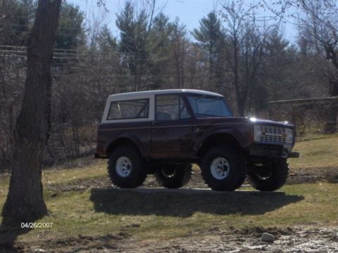 1973 Ford Bronco - A classic 1973 Ford Bronco sits on a raised surface outdoors, with a wooded area behind it.