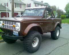 1973 Ford Bronco - Brown 1973 Ford Bronco with a white roof and large tires sits on a residential street.