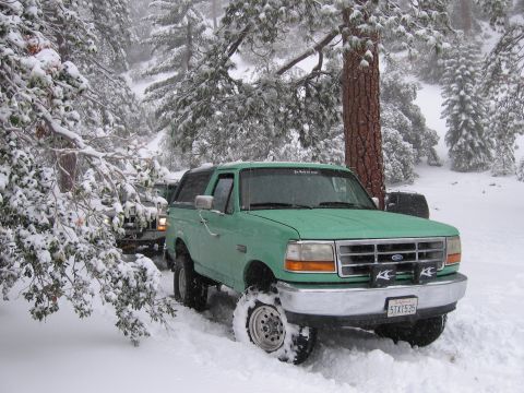 1996 Ford Bronco - A green Ford Bronco navigates a snowy forest road, with another vehicle partially visible behind it.