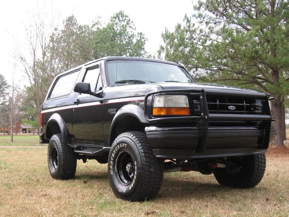 Black two-door full-size Ford Bronco 4x4 with brush guard and Mastercraft A/T tires on grass