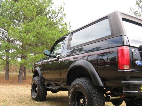 1967 Ford Mustang - Black Ford Bronco parked on grass with trees. The vehicle is viewed from the rear quarter panel.
