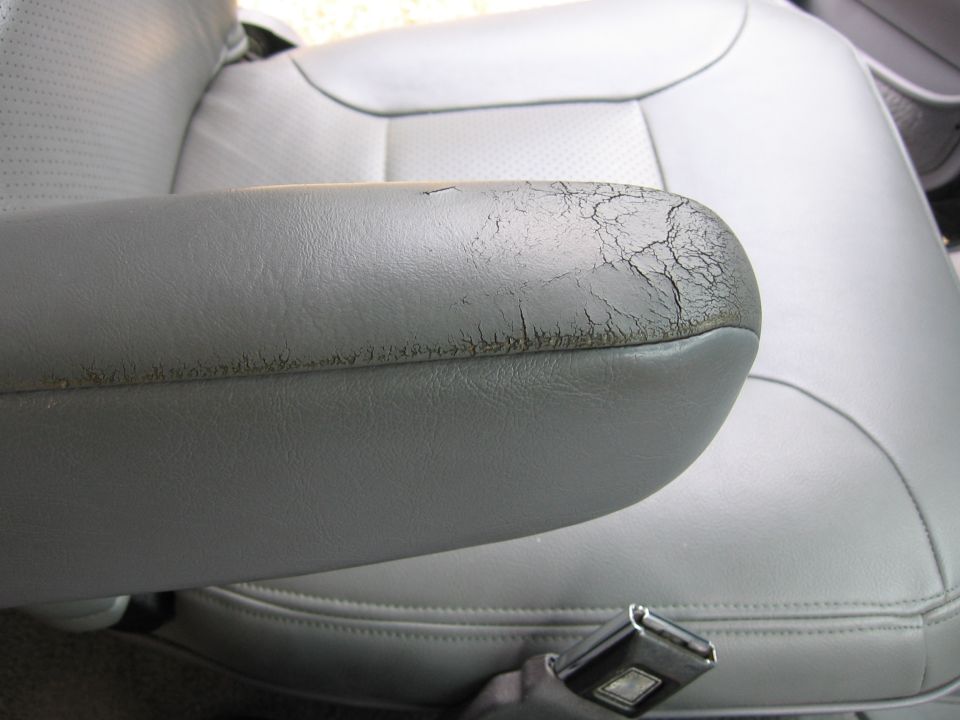 Close-up of a cracked gray leather car armrest with visible wear and tear