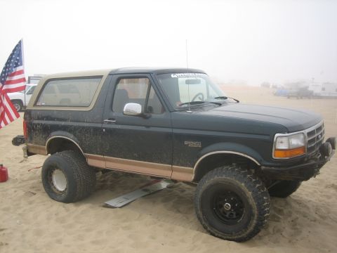 1995 Ford Bronco - Modified 1995 Ford Bronco parked on a sandy beach with an American flag nearby.