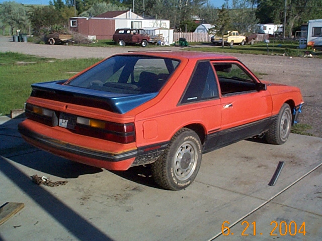 Orange 1983 Mercury Capri hatchback with rear spoiler, seen from rear passenger side on a trailer
