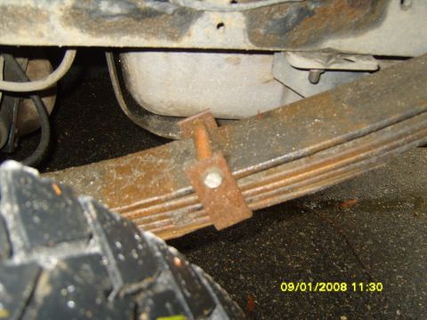 1989 Ford Bronco - Close-up of a rusty leaf spring assembly with a U-bolt clamp and part of a tire visible.