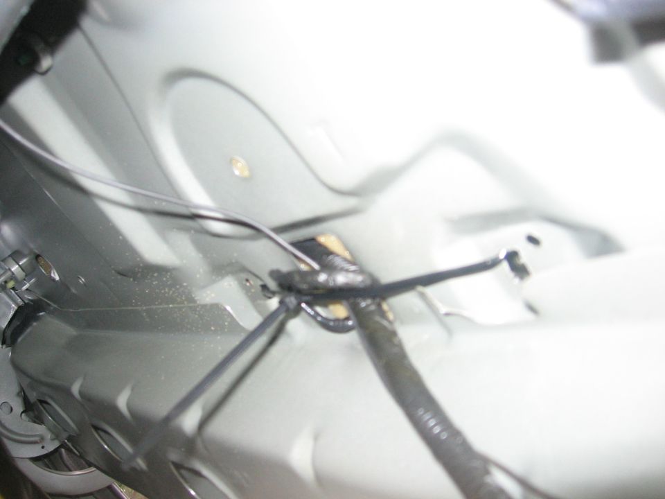 Underbody wiring harness with black tape and zip ties, silver metal paneling visible
