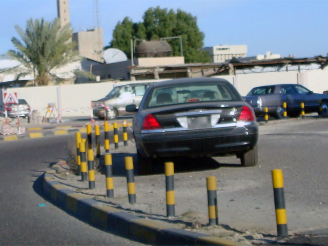 Black sedan parked behind yellow and black bollards, rear view