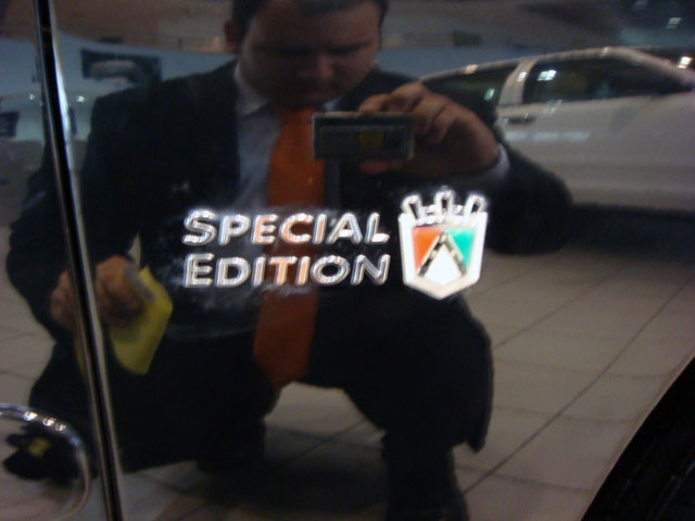 Man in suit and tie polishing a car door, reflecting "Special Edition" badge and another car