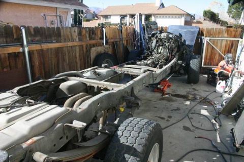 1991 Ford Bronco - The frame of a vehicle is shown with its engine and drivetrain components, undergoing work in a yard.