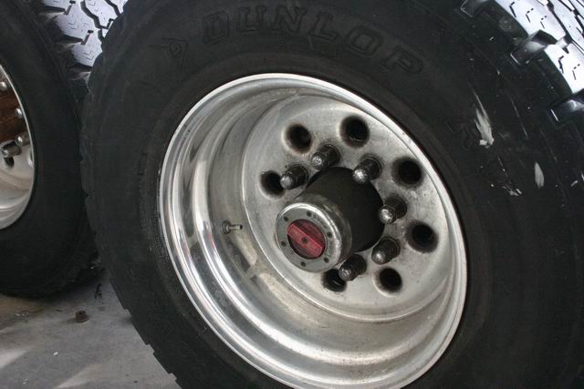 Close-up of two large truck tires and shiny aluminum wheels. One wheel has a red center cap