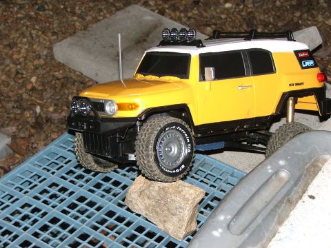 1996 Ford Bronco - This yellow toy FJ Cruiser is positioned on a blue grate with a rock, roof lights and visible text on the tire.