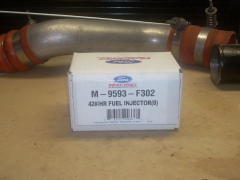 1991 Ford Mustang - Ford Racing performance parts, including fuel injectors and intake piping, are displayed on a workbench.