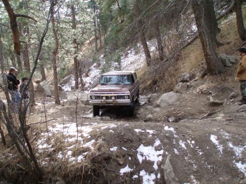 1979 Ford Bronco - This SUV appears to be from the early 1970s, possibly a Ford Bronco, as it tackles a challenging off-road path in a wooded area.