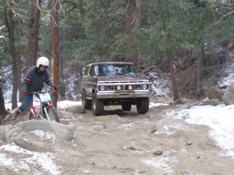 1979 Ford Bronco - A person on a dirt bike navigates a snowy, rocky path as a vintage Ford Bronco drives past.