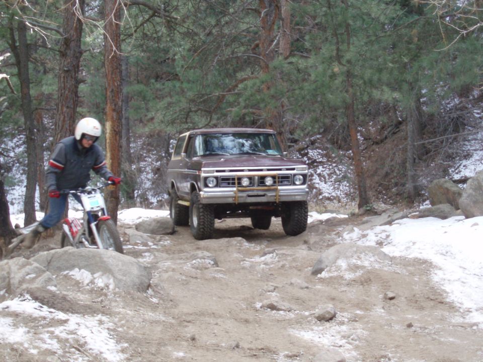 Brown Ford Bronco driving on a rocky, snowy trail with a person on a dirt bike nearby