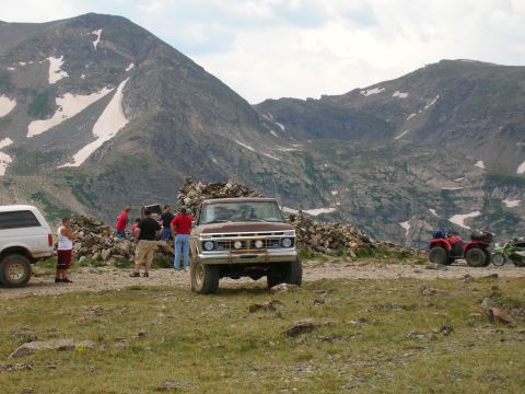 1979 Ford Bronco - A brown pickup truck is parked in a mountainous area with several people gathered nearby. Two ATVs are also visible.