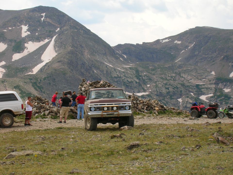 Brown 1973 pickup truck front view with a group of people and mountains behind