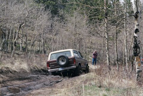 1979 Ford Bronco - A maroon and white Ford Bronco navigates a muddy, wooded trail.