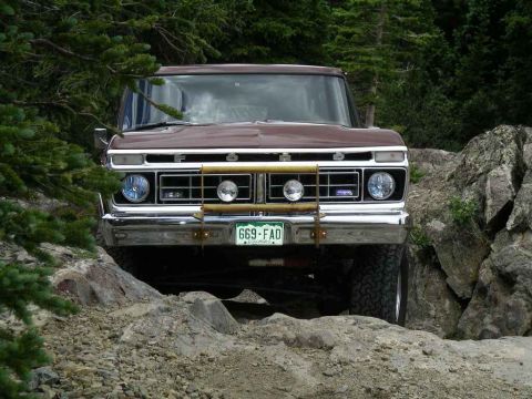 1979 Ford Bronco - Brown Ford F-Series truck with a push bar driving on a rocky mountain trail.