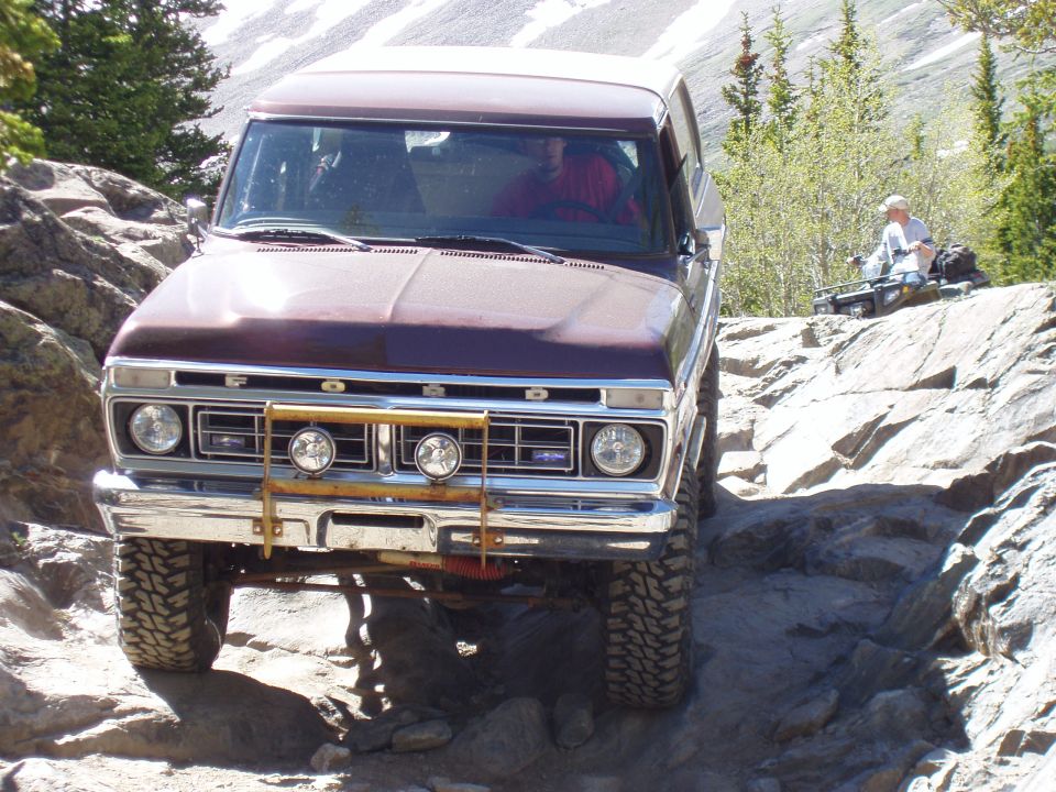 Brown 1979 Ford Bronco on rocky trail with ATV in background