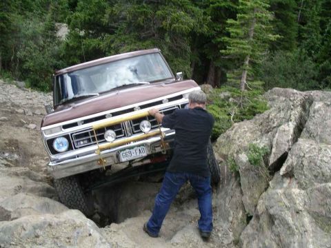 1979 Ford Bronco - A man helps guide a vintage Ford truck over a difficult rocky obstacle on an off-road trail.