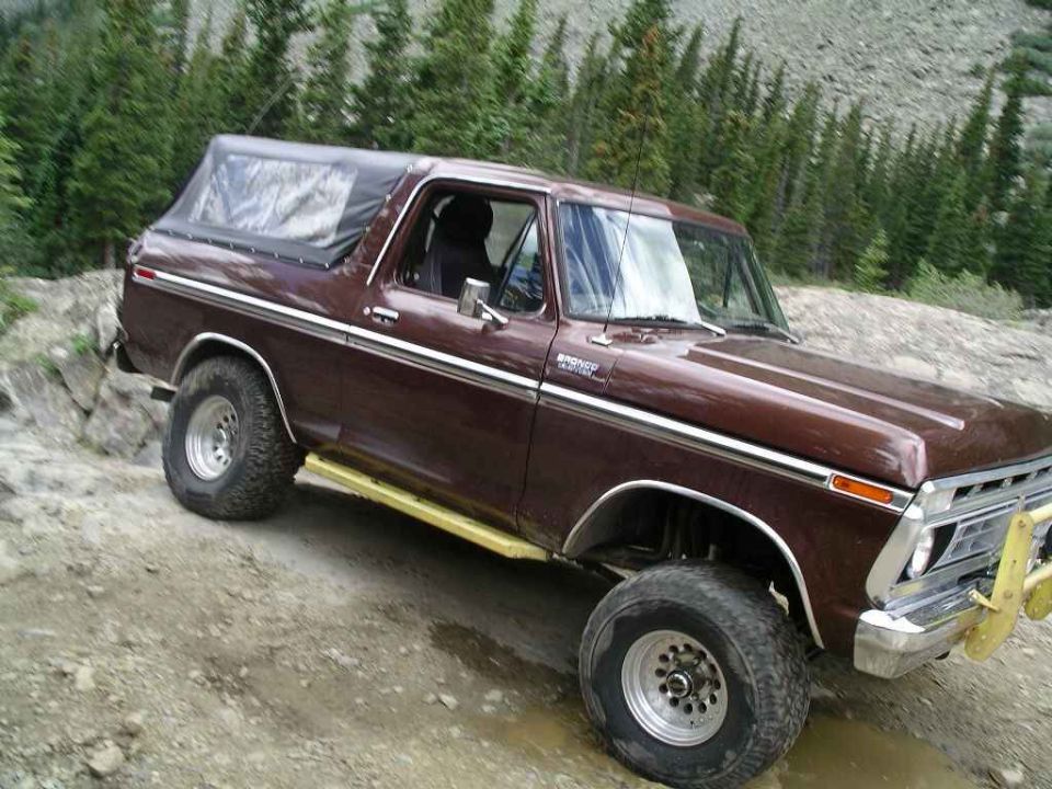 Brown 1978 Ford Bronco with a black soft top and yellow side steps on a dirt road