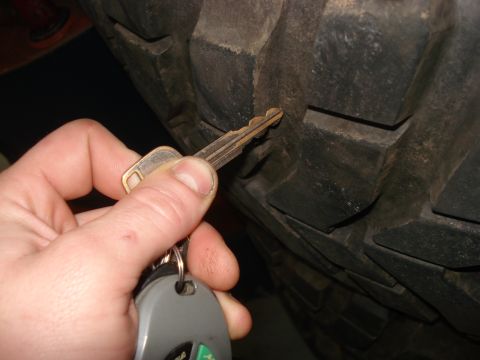 1994 Ford Bronco - A key is shown being inserted into the deep tread of a large tire, possibly indicating a lock or a measurement.