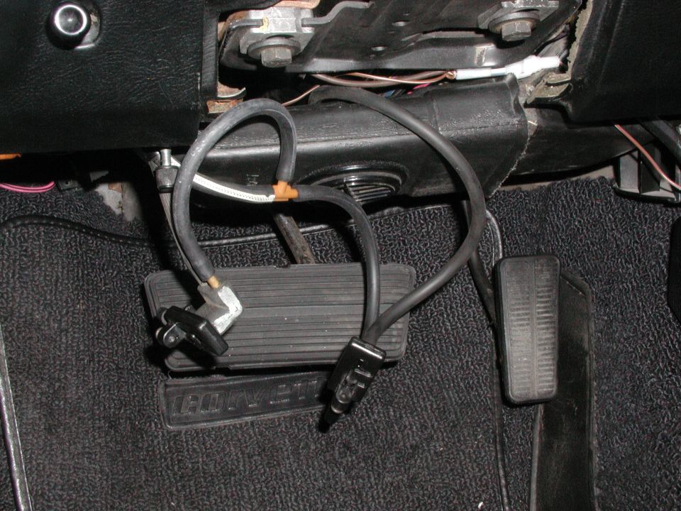Car interior showing brake and accelerator pedals with black hoses and wiring attached
