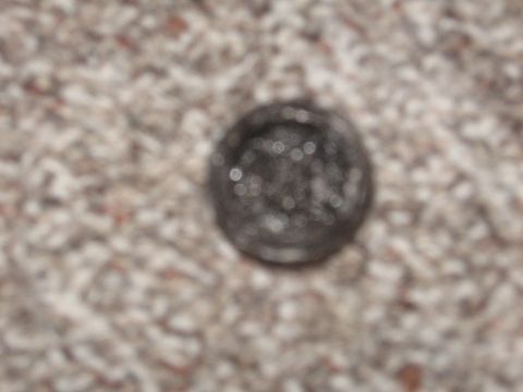 1979 Ford Bronco - A close-up of a dark metal cap with a circular pattern is shown against a speckled carpet background.