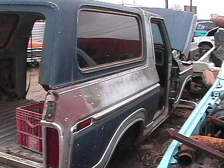 1979 Ford Bronco - A 1979 Ford Bronco is shown with its hood open, surrounded by other vehicles and parts in an outdoor setting.