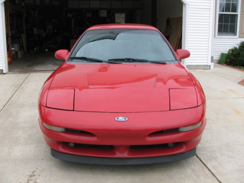 1993 Ford Probe - A red 1993 Ford Probe is parked in front of a garage, showing its distinctive pop-up headlights.