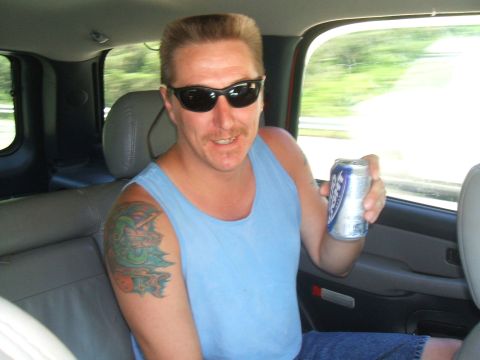 1974 Ford Ranchero - Man with sunglasses and a tattoo on his arm holds a can while sitting in the passenger seat of a vehicle.