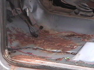1979 Ford Bronco - The interior floor pan of the vehicle shows extensive rust damage and exposed wiring.