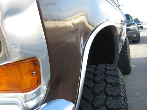 1979 Ford Bronco - Close-up of a brown 1978 Ford Bronco's front fender and wheel, showing off-road tires and chrome accents.