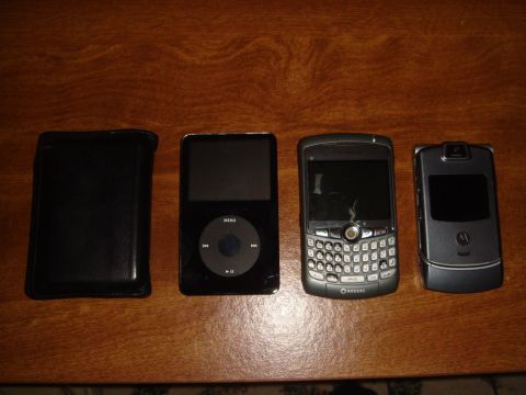 1996 Ford Bronco - A collection of electronic devices, including an iPod, a BlackBerry, and a Motorola RAZR, are laid out on a wooden table.