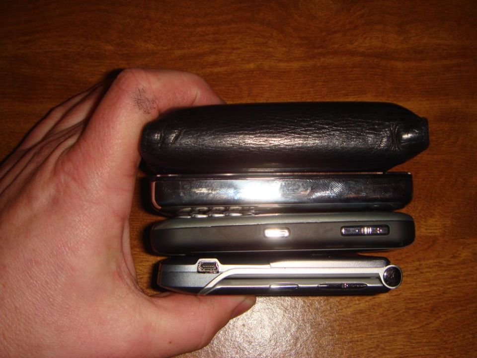 Hand holding a stack of four cell phones, one with a black leather case
